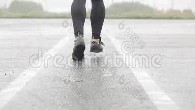 运动鞋跑步者腿的慢动作镜头。 男运动员在户外慢跑。 多雨的单跑道